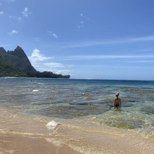 An ocean view of a woman in the water and mountains to the left